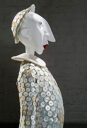 Profile from waist up of puppet with white face in costume made from large pearl buttons